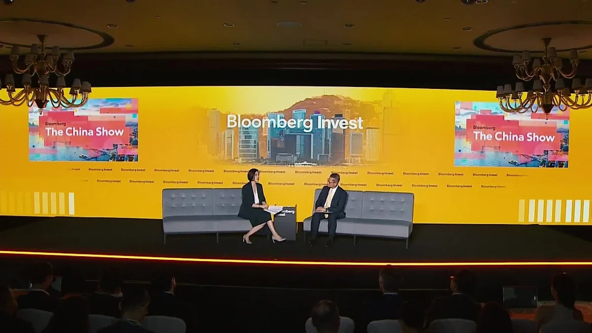Two speakers on a stage with a large screen displaying 'Bloomberg Invest The China Show'