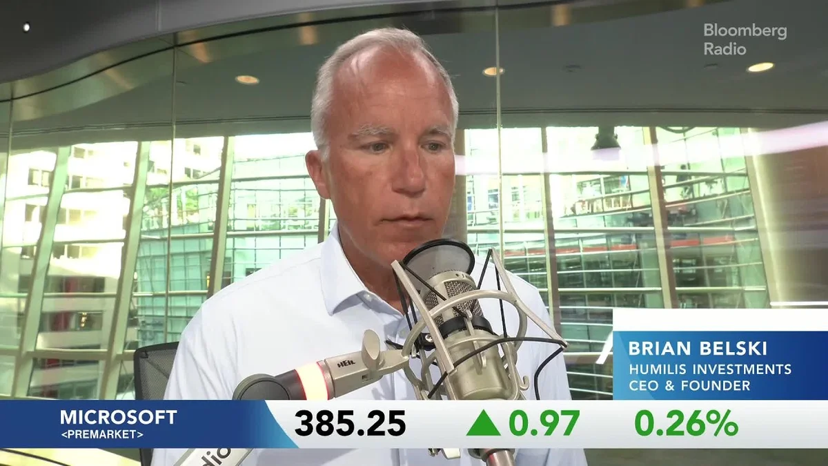 Two men in a broadcast studio discussing financial markets, with stock tickers displayed.