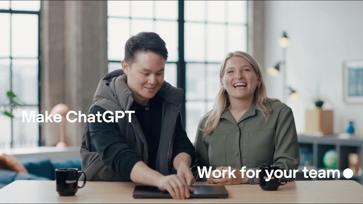 Two people sitting at a table with a laptop showing the OpenAI logo.